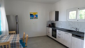 A kitchen with a dining table, chairs, a refrigerator, cabinets, a window, and a painting on the wall.