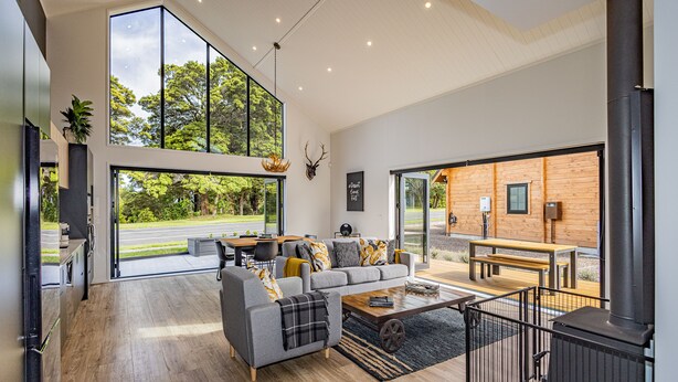 A spacious living area with a large window, a fireplace, and a dining area. - Mangawhero River Chalet (Ohakune)
