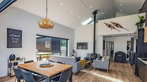 A modern living space with a wooden dining table, grey sofas, and a large window. - Mangawhero River Chalet (Ohakune)