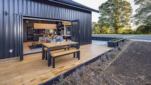 A modern building with a wooden deck, a kitchen area, and a seating area with a table and chairs. - Mangawhero River Chalet (Ohakune)