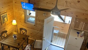 Interior d'una cabana de fusta amb zona de dinar, cuina i televisió penjada a la paret.