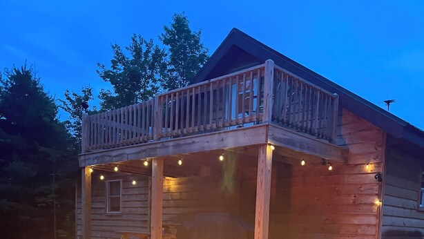 Una cabana de fusta amb un porxo, dues cadiretes Adirondack i una xemeneia.