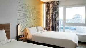 A hotel room with two beds, a nightstand with a lamp, a wall art piece, and a large window with a city view. - B&B HOTEL Paris Ivry Quai de Seine (Ivry-sur-Seine)