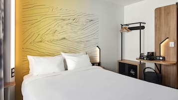 Habitación de hotel con cama, cabecero de pared, mesita de noche, armario, perchero y estante pequeño con radio y teléfono.