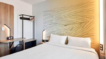 Moderni hotellihuone, jossa on sänky, yöpöydät, työpöytä ja seinälle kiinnitetty naulakko.