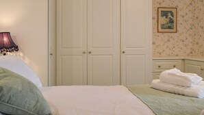Ein Schlafzimmer mit einem Bett, einem Kleiderschrank, einer Nachttischlampe und einem gerahmten Bild an der Wand.