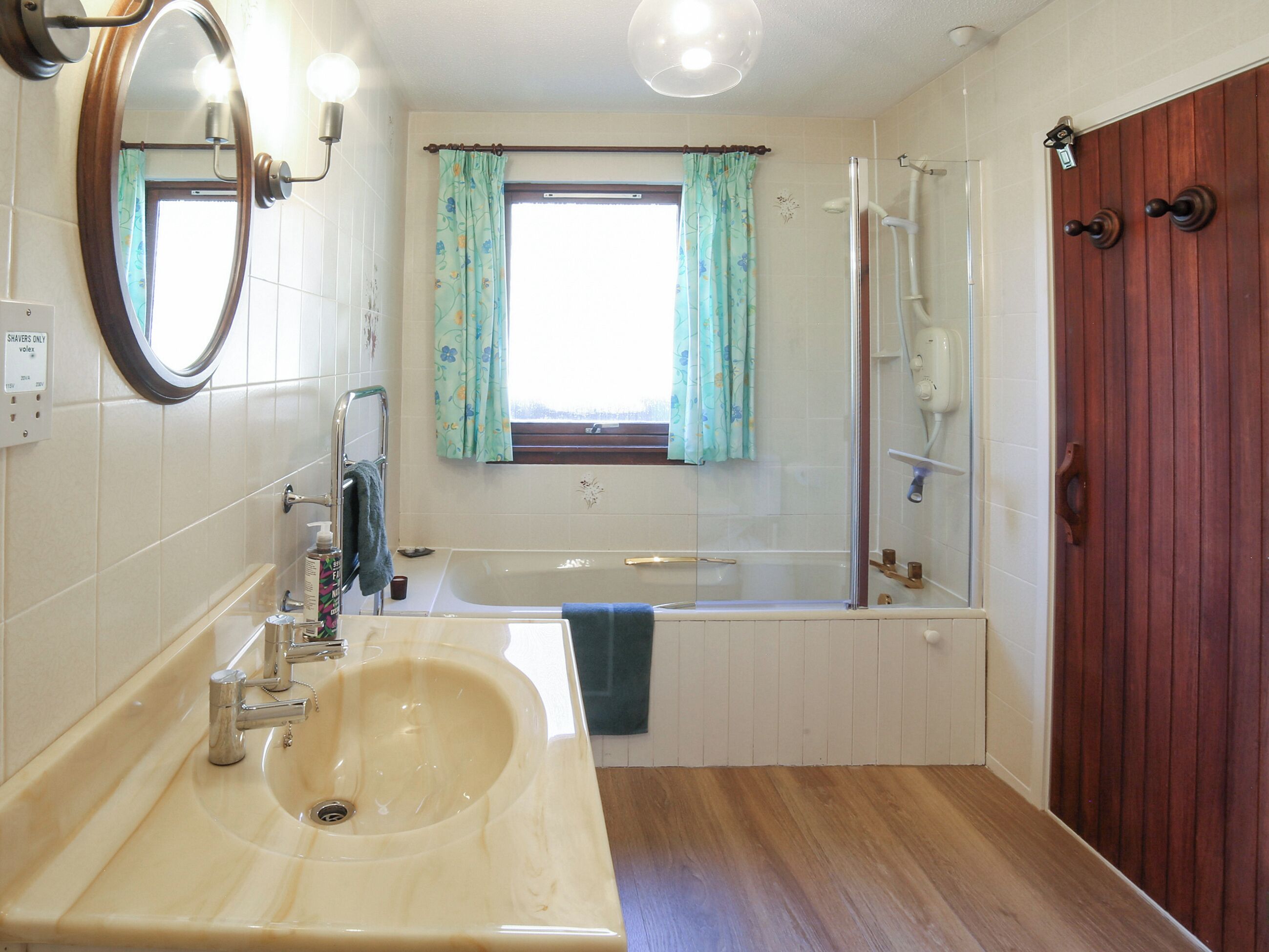 Ein Badezimmer mit Waschbecken, Spiegel, Dusche und einer Holztür.