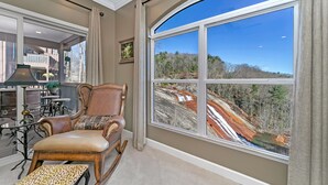 A room with a large arched window, a rocking chair, and a view of a forested area.