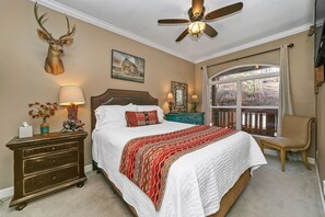 A bedroom with a large bed, a ceiling fan, a mounted deer head, and a window with a view of trees. - Lake Toxaway Falls: Waterfall Views, Luxury Condo, minutes from hiking! (Lake Toxaway)