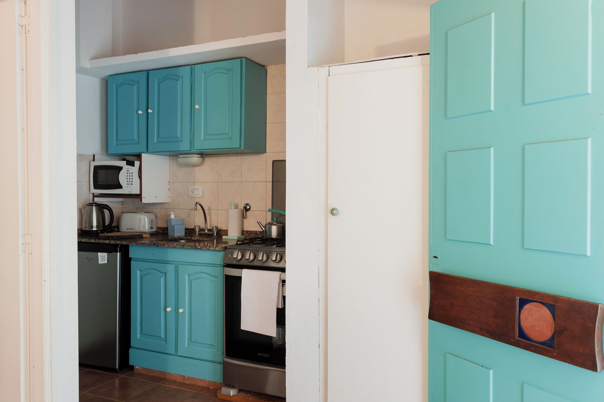 A kitchen with teal cabinets, a white microwave, a stove, and a dishwasher.