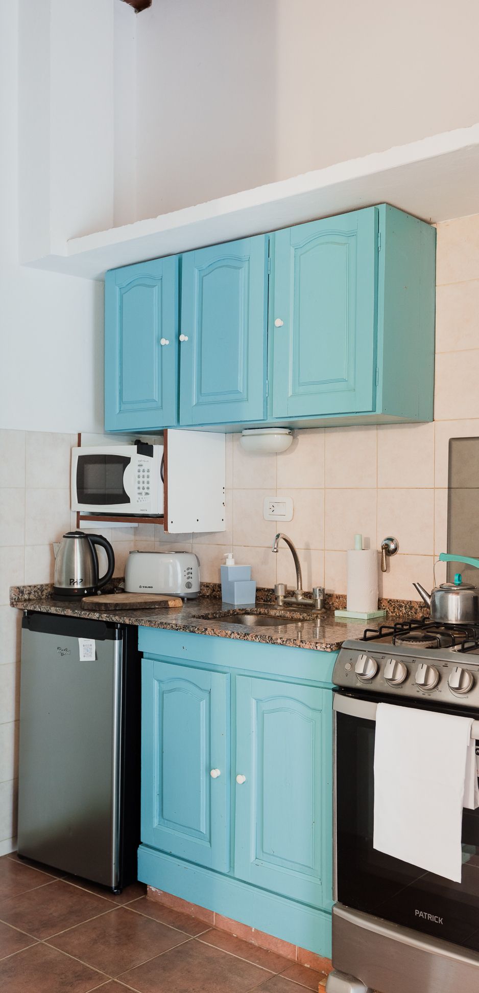 A kitchen with teal cabinets, a microwave, a toaster, a kettle, a dishwasher, and a stove.