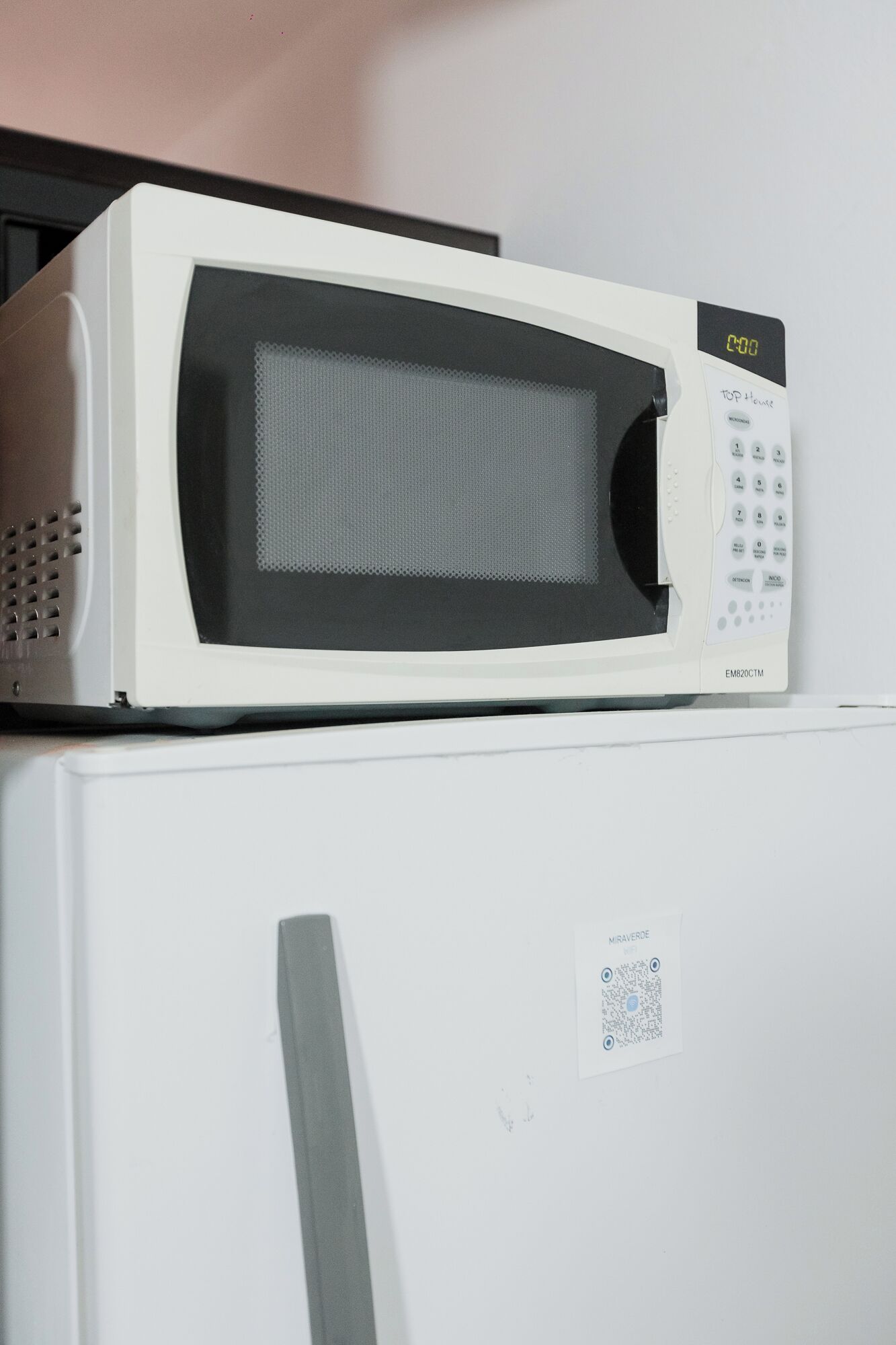 A white microwave oven with a digital display and keypad on top of a white refrigerator.