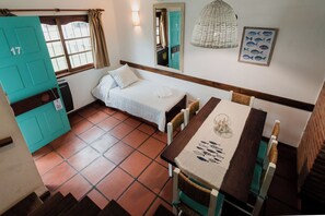 A room with a bed, a table with chairs, a door, a window, and a wall-mounted light fixture.