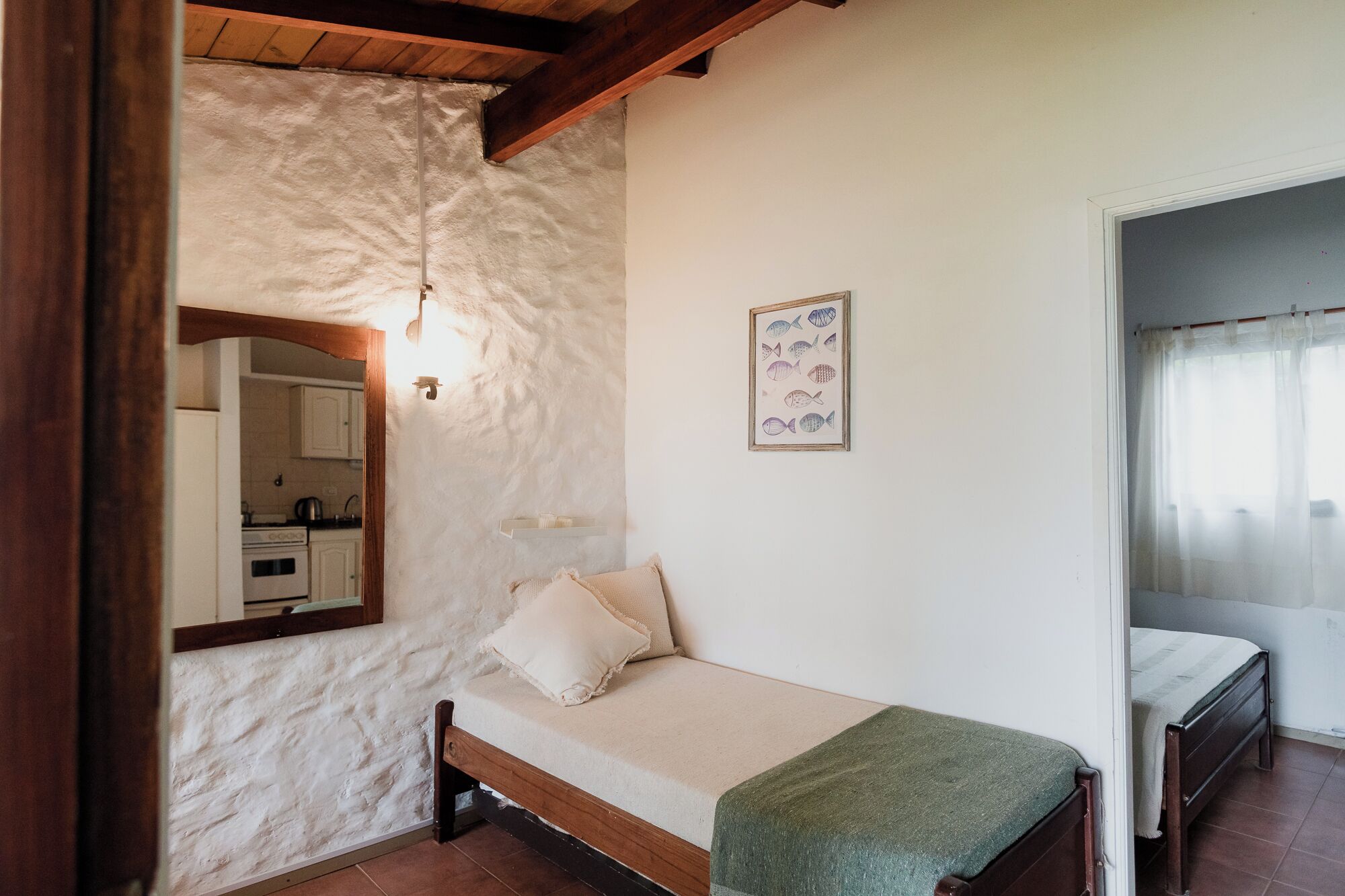Un dormitorio con cama de madera, pared blanca, cuadro de peces enmarco y un espejo.