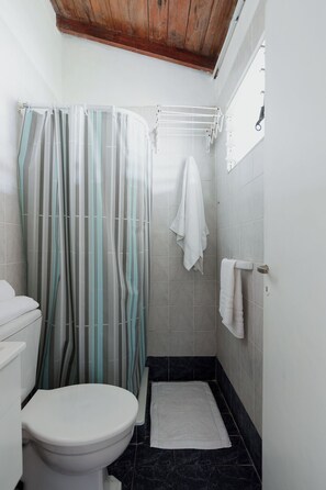 A bathroom with a shower curtain, a toilet, a towel rack, and a small rug.