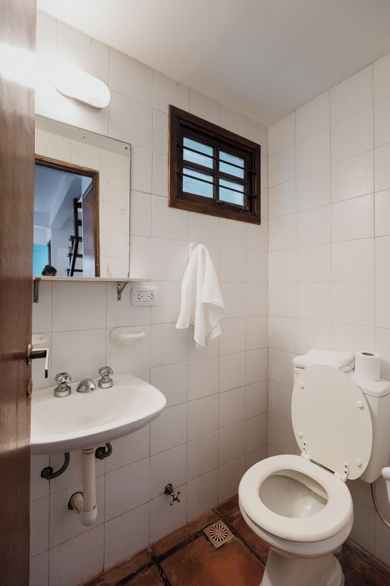 Un baño pequeño con un lavamanos blanco, un espejo, una ventana y un inodoro.