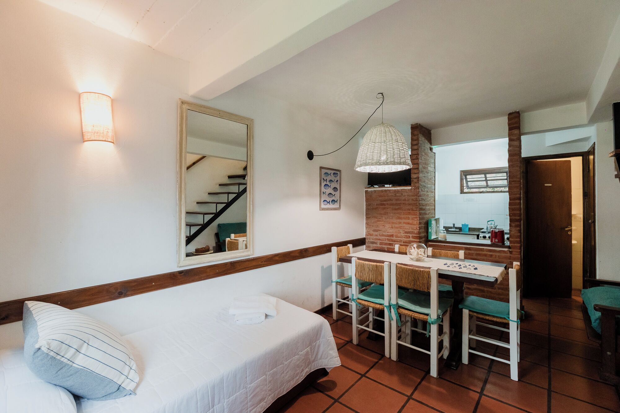 Quarto com cama, escrivaninha com cadeiras, espelho e luminária pendente.
