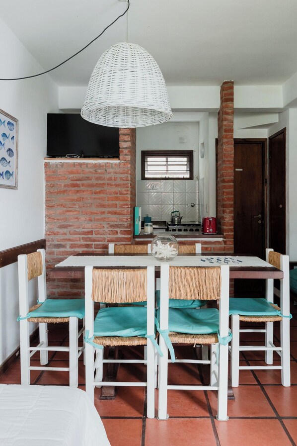 Un coin repas avec une table et des chaises blanches, un luminaire suspendu et un mur en briques.