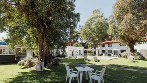 A courtyard with a white table and chairs, surrounded by trees and a building with a red roof. - Miraverde Pinamar (Pinamar)