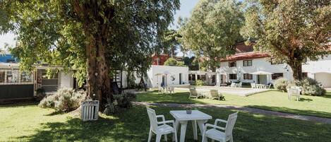 A courtyard with a white table and chairs, surrounded by trees and a building with a red roof.