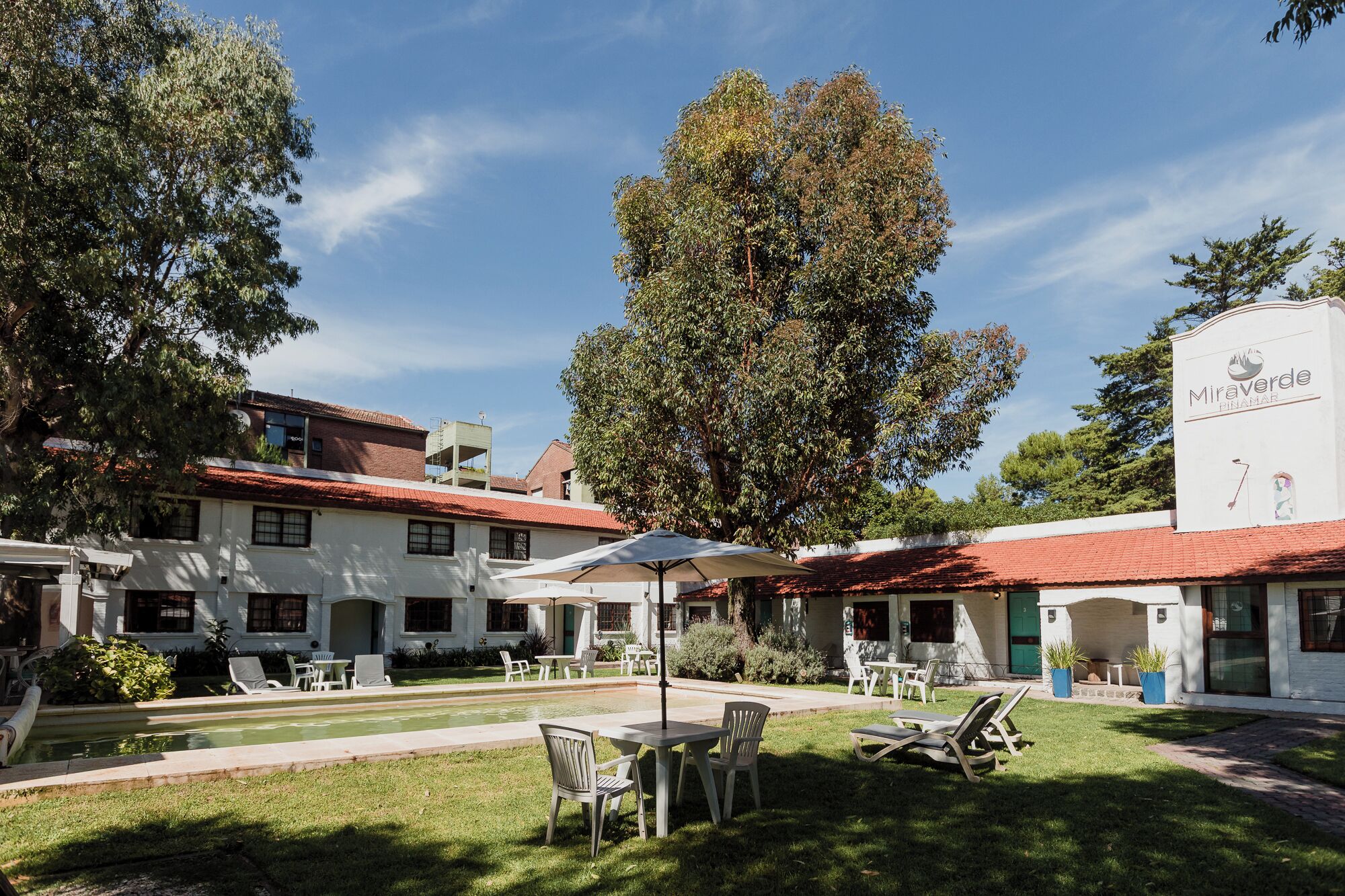 A hotel courtyard with outdoor seating, a pool, and a large tree.