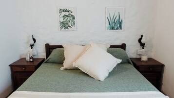 Una cama con una colcha verde y dos almohadas, flanqueada por mesitas de noche con lámparas de pared y una botella pequeña en cada una.