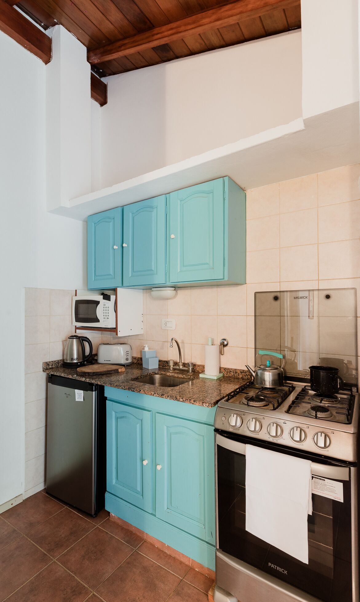 A kitchen with teal cabinets, a microwave, a sink, a refrigerator, a stove, and a tiled backsplash.