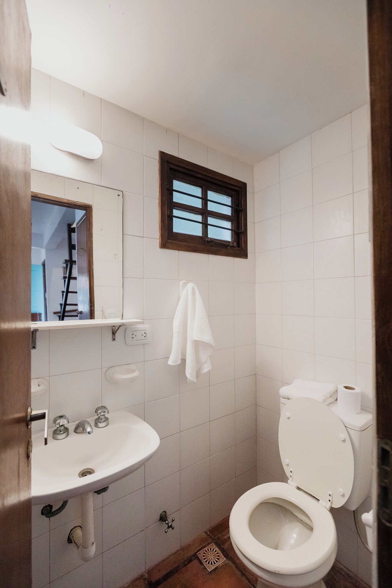 A small, clean bathroom with a white sink, a toilet, and a window with blinds.