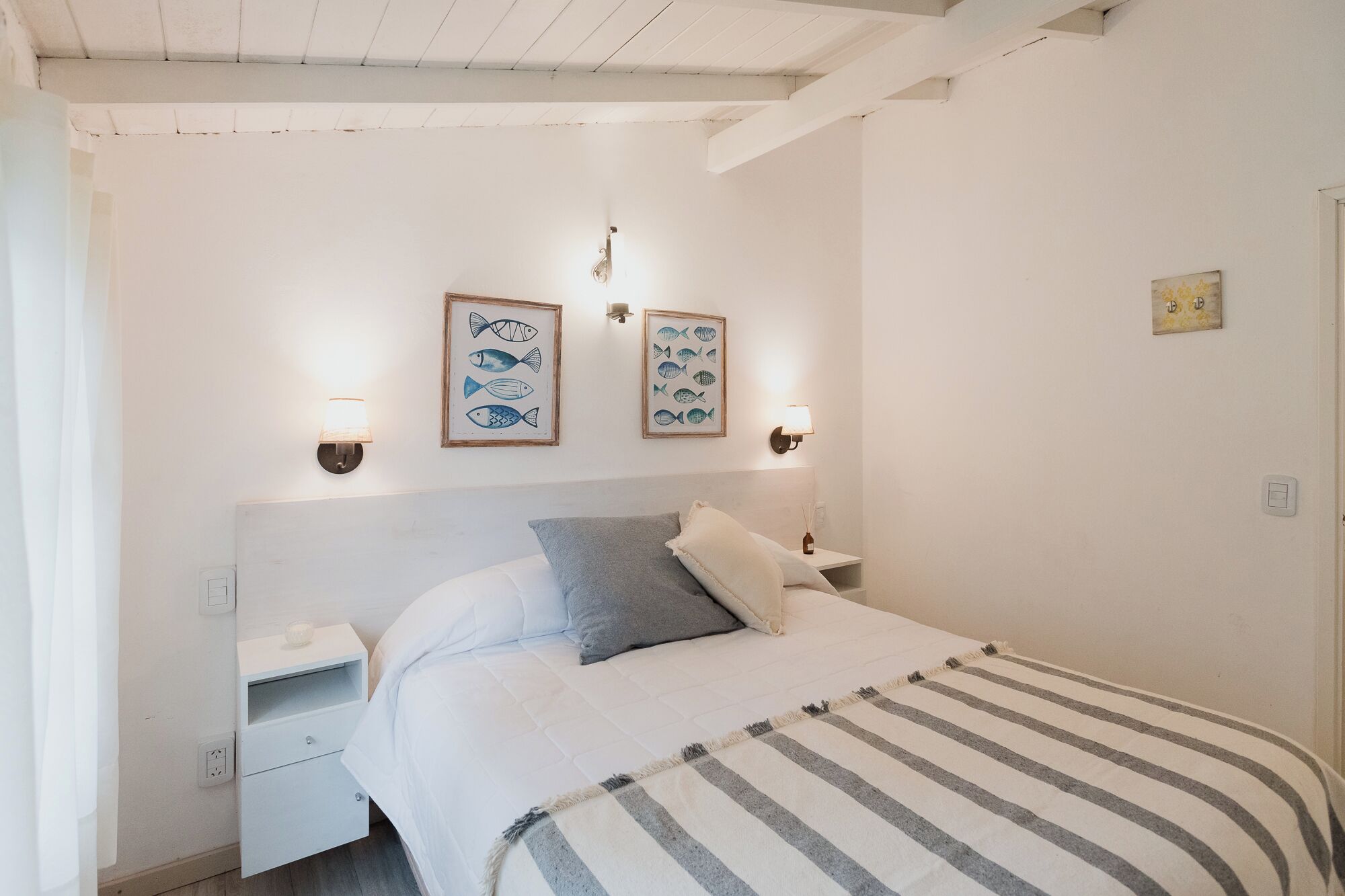 Een slaapkamer met een bed, twee wandlampen en twee kunstwerken van vissen in lijsten.