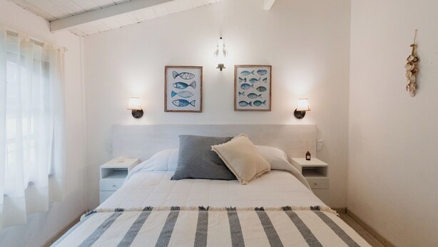 A bedroom with a bed, two bedside tables, a nightstand, a striped rug, and two wall-mounted lamps. - Miraverde Pinamar (Pinamar)