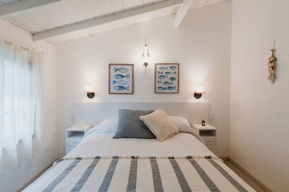 A bedroom with a bed, two bedside tables, a nightstand, a striped rug, and two wall-mounted lamps.