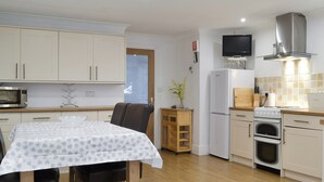 A compact kitchen with white cabinets, a microwave, a refrigerator, a stove, and a small dining area with a table and chairs.
