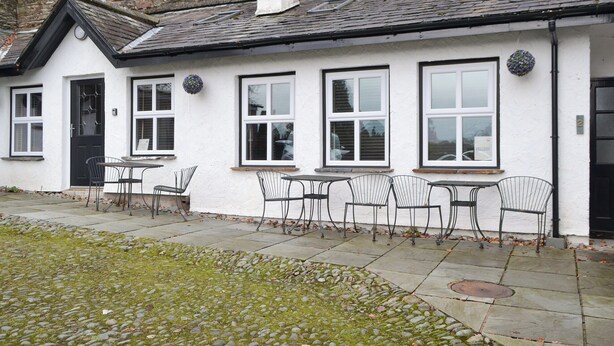 A white building with a black door, multiple windows, and outdoor seating with metal chairs.