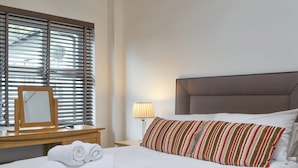 A neatly made bed with white linens, a striped pillow, and rolled towels on a wooden nightstand.