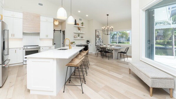 A modern kitchen with white cabinetry, a large island with bar stools, and a dining area with a bench and chairs.