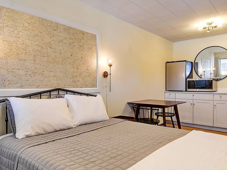 A bedroom with a bed, bedside table, wall-mounted light, and a small table with chairs.