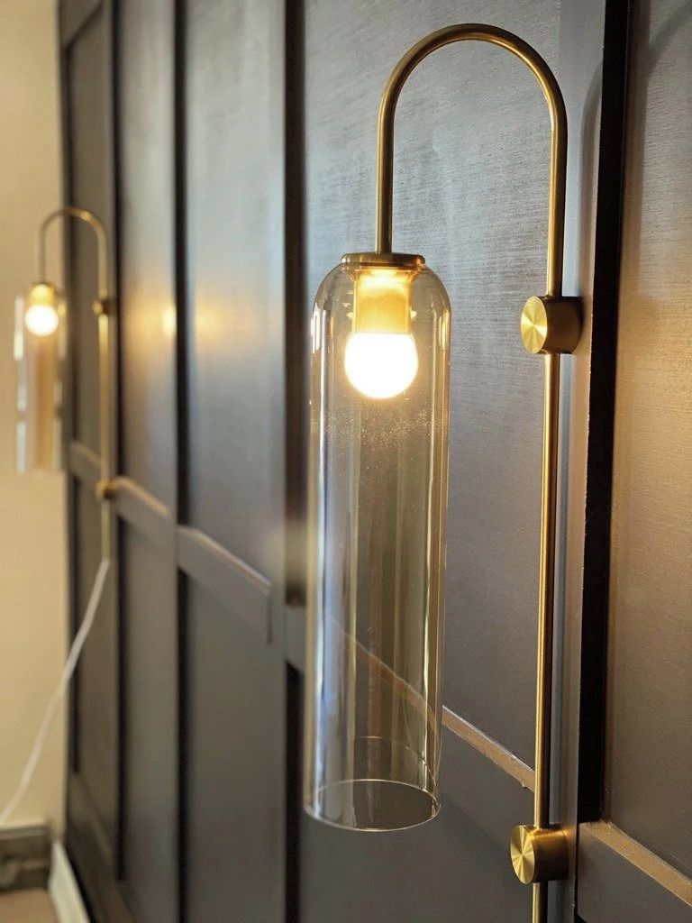 Una lámpara de pared con una carcasa de vidrio transparente y un brazo metálico curvo.