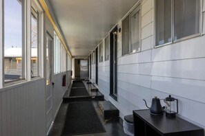 A corridor with a black mat leading to a door, a fire extinguisher, and a table with a coffee pot and a lantern.