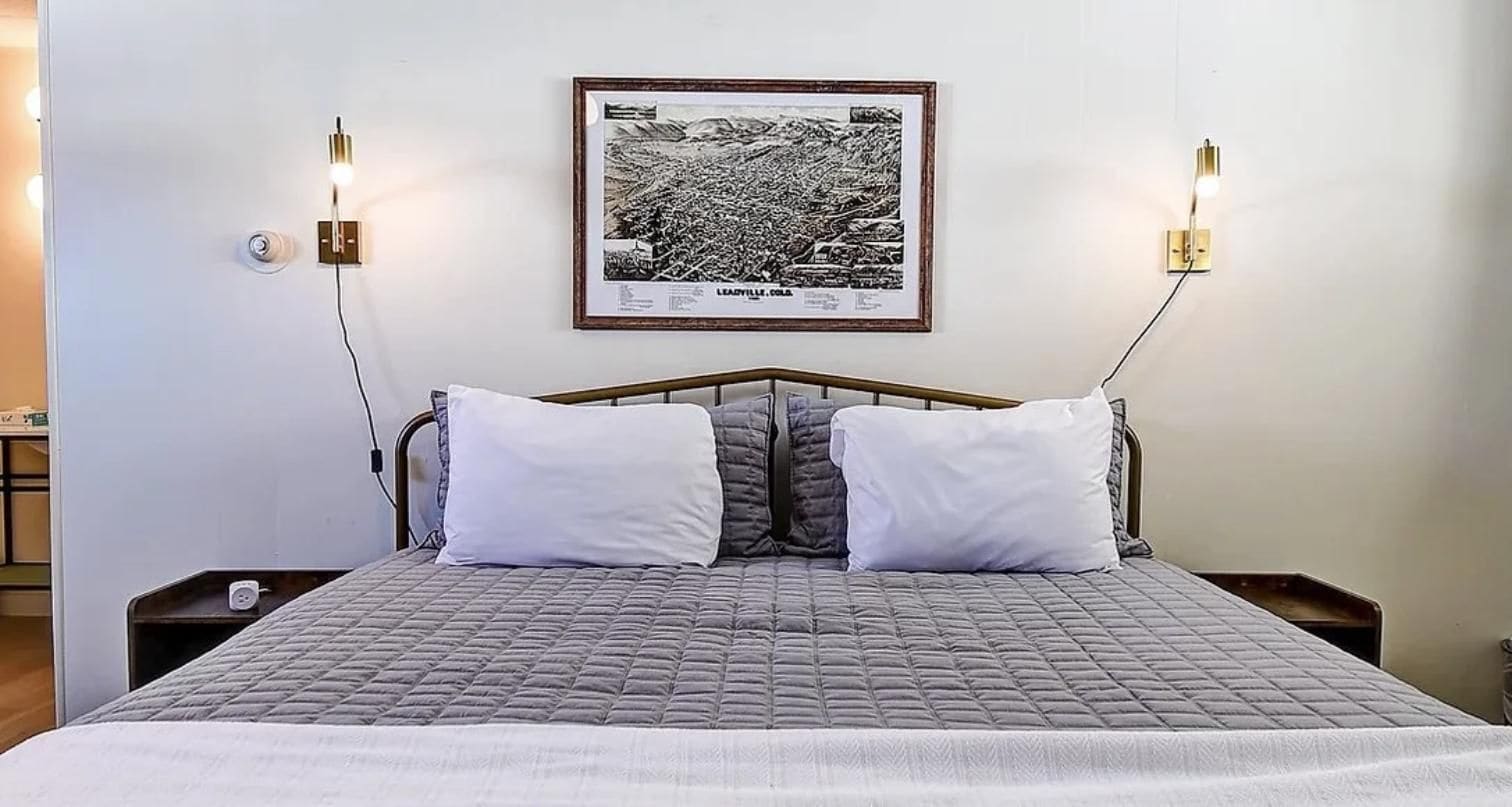 A bed with a quilted gray bedspread, two white pillows, and a framed black and white photograph on the wall.