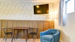A room with a wooden table, four chairs, a blue armchair, a flat-screen TV mounted on the wall, and a window with curtains. - Old Tale Inn (Leadville)