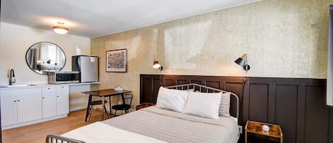 Un dormitorio con cama, mesita de noche, lámpara y una kitchenette con refrigerador y microondas.