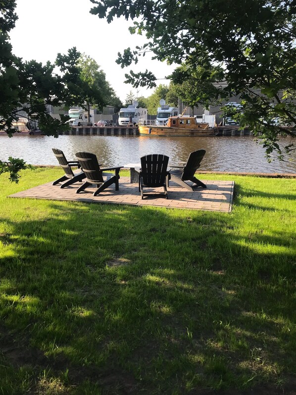 Un espacio con césped, una mesa y cuatro sillas Adirondack mirando al agua.