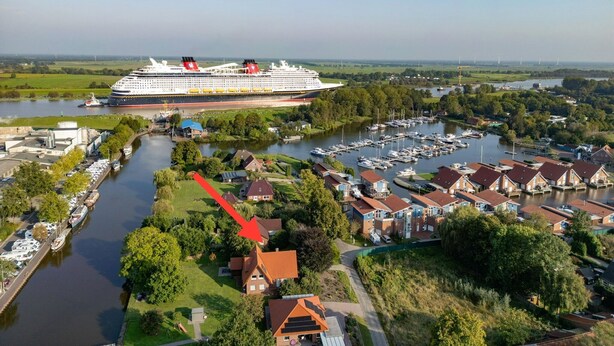 Un gran crucero atracado en un puerto con un puerto deportivo lleno de barcos, rodeado de edificios residenciales y zonas verdes.