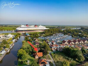 Un grand navire de croisière a accosté dans un port doté d’une marina remplie de bateaux, entourée de bâtiments résidentiels et de verdure.