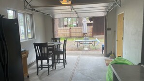 Un garaje con una mesa, sillas, un refrigerador y un bote de basura verde.