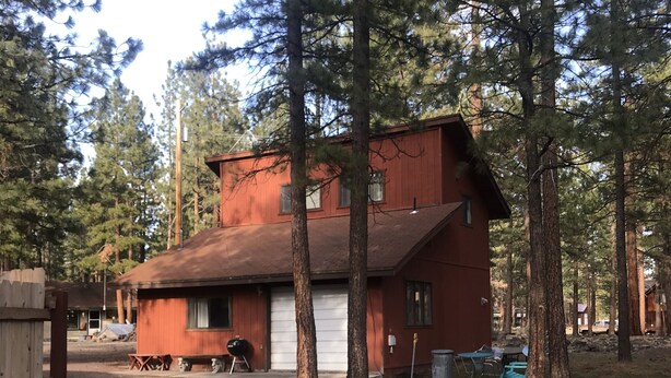 Una cabaña de dos pisos con fachada roja, rodeada de altos pinos.