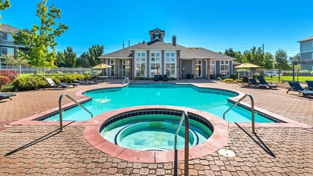 A swimming pool with a hot tub, lounge chairs, and a building with a large window in the background.