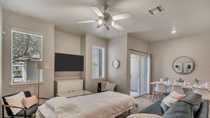 A modern bedroom with a bed, a gray sofa, a dining table with chairs, and a ceiling fan.