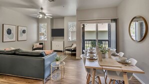 A modern living room with a sofa, a dining table set for four, and a ceiling fan.