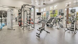 A gym with various exercise equipment, large windows, and a ceiling fan.
